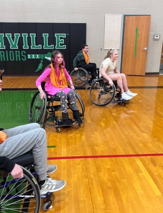 Students wheel around gym in wheelchairs